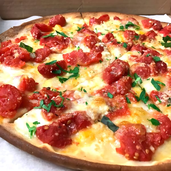 Close-up of a Classica Pizza with diced tomatoes, melted cheese, and fresh herbs in a box.