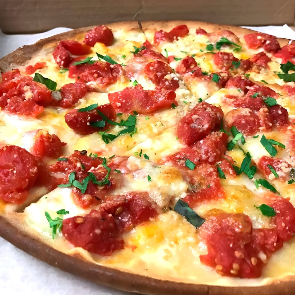 Close-up of a Classica Pizza with diced tomatoes, melted cheese, and fresh herbs in a box.