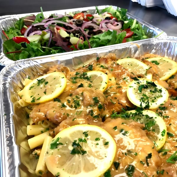 Chicken piccata with pasta and a fresh garden salad in aluminum catering trays.