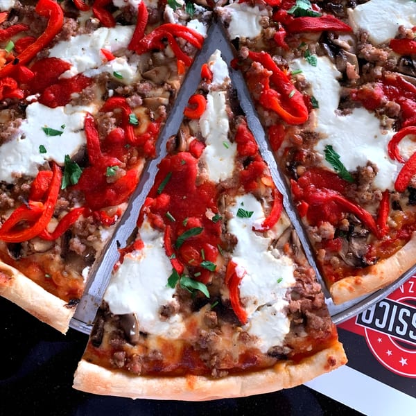 Classica Pizza with red peppers, sausage, mushrooms, and dollops of ricotta cheese, with a slice removed.