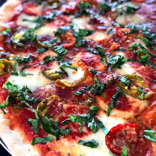 Close-up of a Classica Pizza with tomato sauce, melted cheese, basil, and sliced peppers.
