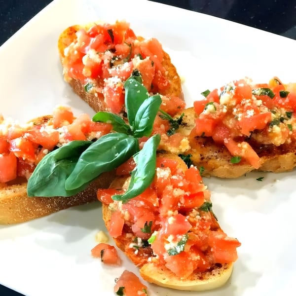 Four bruschetta pieces with diced tomatoes, cheese, and basil on a white plate.