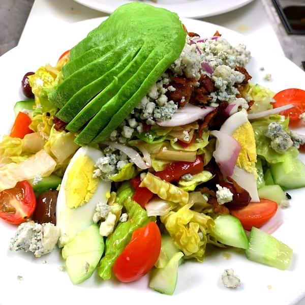 A vibrant Classica Pizza salad with avocado, bacon, blue cheese, tomatoes, eggs, and lettuce.